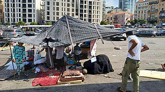 Menschen unter einer provisorischen Plane auf einem Parkplatz