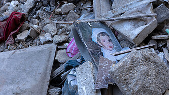 Trümmerteile von Häusern liegen auf dem Boden, darin liegt ein Bild von einem Kind
