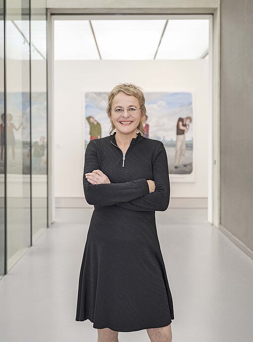 Ein blonde Frau mit schwarzem Kleid steht in einem weiß lackierten Ausstellungssaal