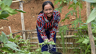 Frau gießt Gemüsepflanzen in einem nachhaltigen Gartenprojekt in Laos