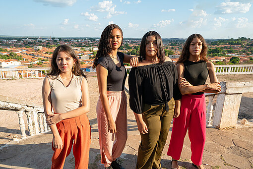 Vier jugendliche Mädchen aus Brasilien stehen selbstbewusst zusammen und blicken in eine Kleinstadtlandschaft, ein Symbol für Bildung und Gemeinschaft.