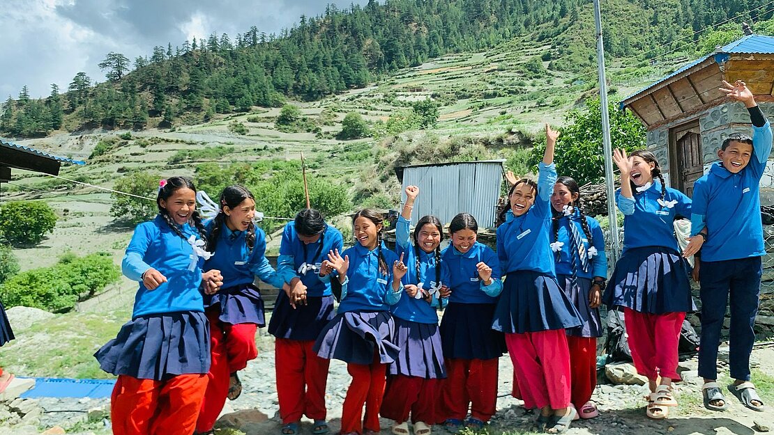 Schulkinder aus Nepal in blauen Schuluniformen beim Spielen im Freien vor einer hügeligen Landschaft