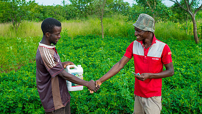 Ein Mann gibt einem anderen Mann die Hand, er verkauft sein Pflanzenschutzmittel und der andere Mann gibt ihm dafür Geld.