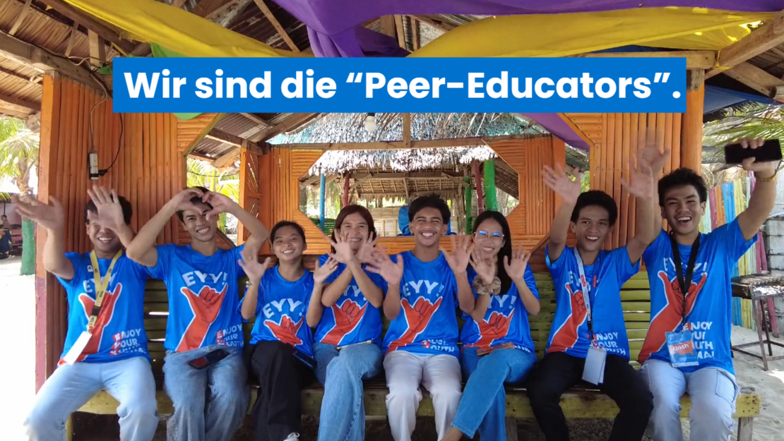 Acht Jugendliche aus den Philippinen sitzen als Peer-Educators in einem bunt geschmückten Holzpavillon, tragen blaue T-Shirts und winken fröhlich in die Kamera. Der Schriftzug „Wir sind die Peer-Educators“ ist im Bild eingeblendet.
