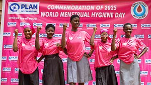 Fünf junge Frauen in pinken T-Shirts von Plan International feiern den Weltmenstruationstag 2025 und heben selbstbewusst die Faust.