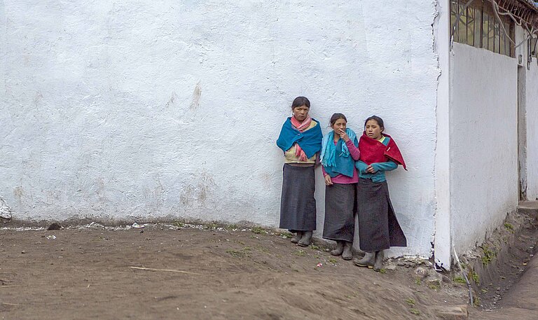 Drei Schulmädchen stehen an der Wand vor ihre Schule in den Anden.