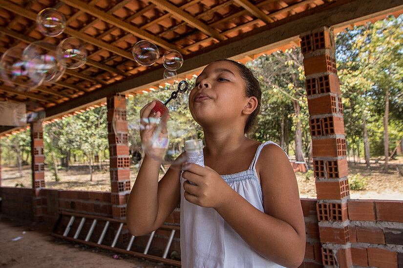 Kind spielt mit Seifenblasen auf einem Projektgelände in Brasilien Mädchen pustet Seifenblasen unter einem überdachten offenen Bau in Brasilien