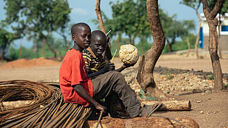 zwei afrikanische Kinder sitzen nebeneinander auf zusammengebundenen, alten Kabeln und schauen in die Kamera.