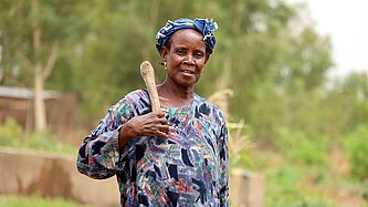 Eine Frau steht mit einem Holzwerkzeug über der Schulter in ihrem Garten