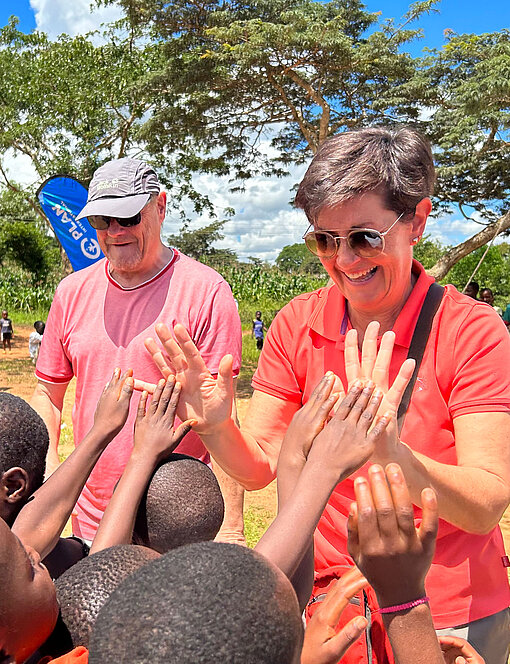 Besuchende geben Kindern High-Fives bei einem Projekttreffen in Malawi.