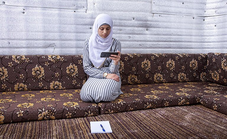 Shayma’a hockt auf einem großen braunen Sofa.