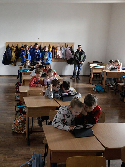 Kinder sitzen in einem Klassenzimmer und schauen jeweils zu zweit auf einen Tablet-Computer