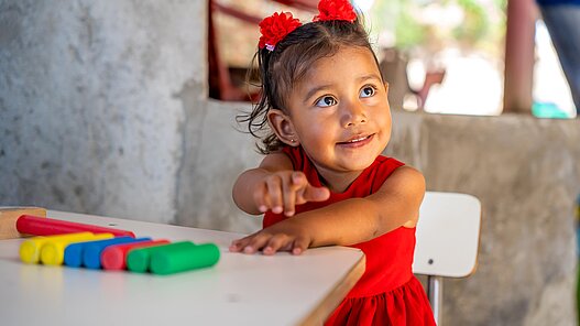 Mädchen aus El Salvador sitzt am Tisch und spielt