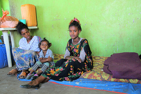 Mutter mit zwei Töchtern sitzt auf Matratze in einfachem Raum mit grün gestrichener Wand in Äthiopien