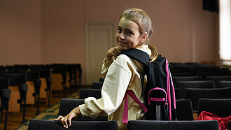 Ein Mädchen mit lila Rucksack schaut lächelnd über ihre Schulter.