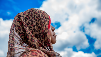 Ein 14-jähriges Mädchen aus Mosambik guckt in den strahlend-blauen Himmel mit weißen Wolken. Sie trägt ein Kopftuch mit Leopardenmuster, das ihr Haar bedeckt. Ihr Gesicht ist nicht zu sehen.