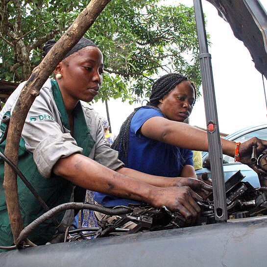 Teninkè und N'Mahaw arbeiten am Motor eines Autos.