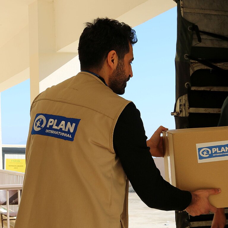 Plan Mitarbeiter bringt ein Paket mit Schulutensilien in den Südlibanon