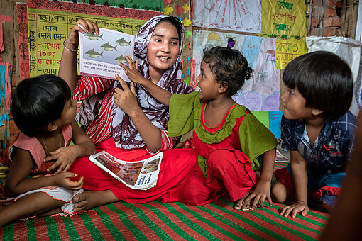 Eine Frau zeigt ein Buch den Kindern vor
