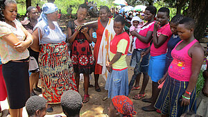 Gruppe von Frauen und Mädchen, die draußen im Schatten eines Baumes stehen und sich unterhalten, ländliche Umgebung
