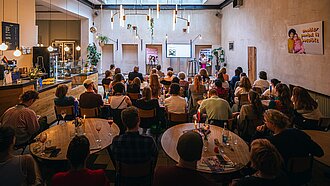 Etwa 50 Menschen sitzen in einem Raum zusammen