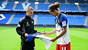 Zwei HSV-Spieler stehen sich im Stadion gegenüber und unterzeichnen ein HSV-Trikot