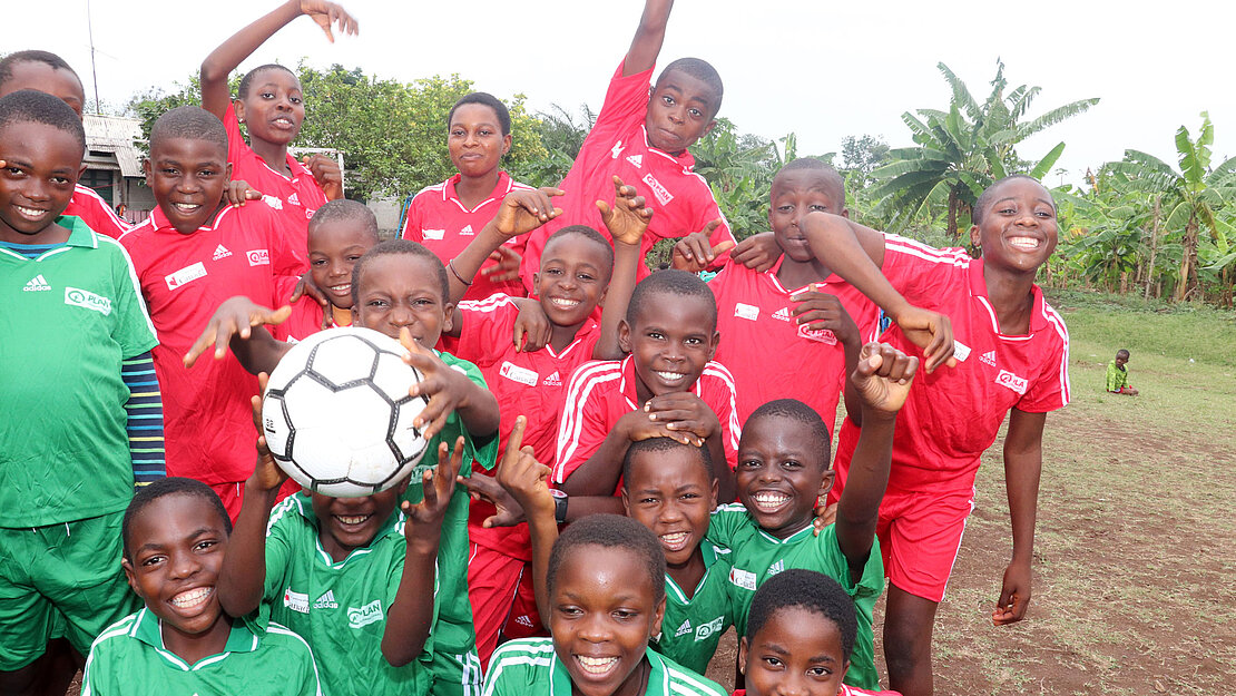 Eine Gruppe Kinder in Fußballtrikots steht für ein Gruppenbild zusammen und macht Blödsinn.