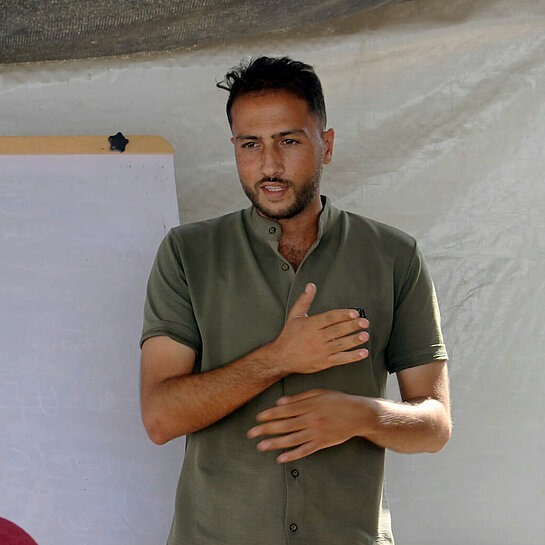 Mohammed steht vor einem Flipboard und spricht zu einer Gruppe Menschen