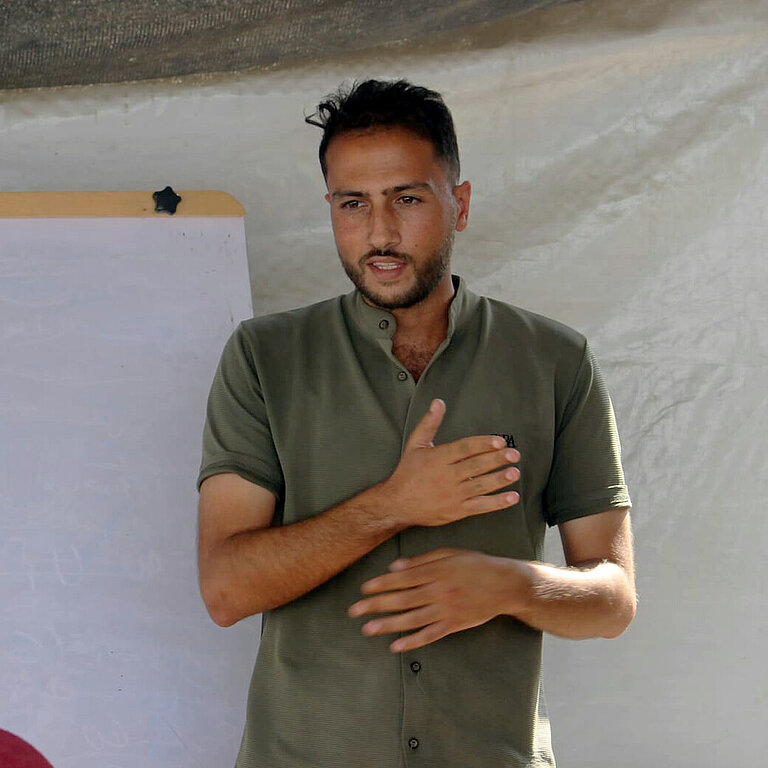Mohammed steht vor einem Flipboard und spricht zu einer Gruppe Menschen