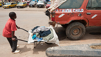 Ein kleiner Junge schiebt Altkleider in einer Schubkarre zum Markt in Tubmanberg, Liberia. ©Plan International/Marc Schlossman