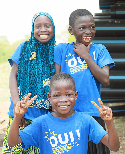 Zwei Jungen und ein Mädchen in blauen T-Shirts lachen in die Kamera