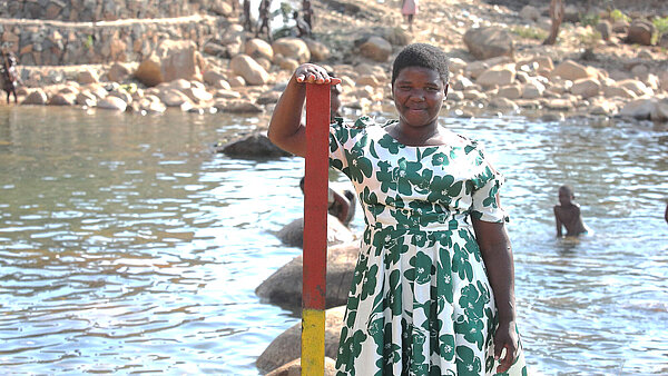 Eine Frau steht am Flussufer und zeigt den Wasserstandmesser, der Menschenleben rettete