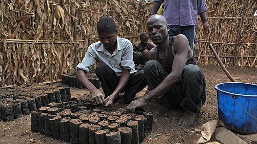 Zwei Männer säen die Baumsamen in vorbereitete Plastiktöpfe aus. Dieses Bild stammt aus einem ähnlichen Plan-Projekt in Malawi.