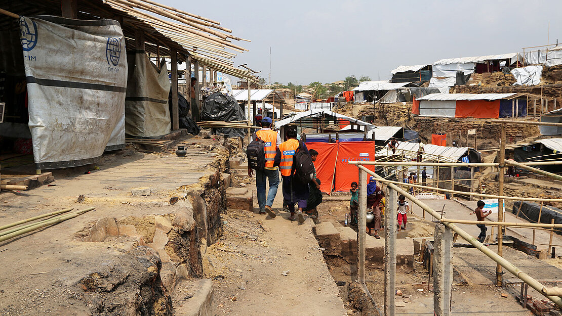 Plan Mitarbeiter laufen durch ein Camp aus provisorischen Gebäuden aus Bambus und Planen.