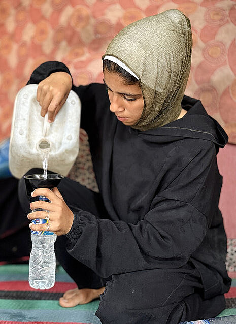 Eine junge Frau befüllt mit einem Kanister Wasserflaschen aus Plastik
