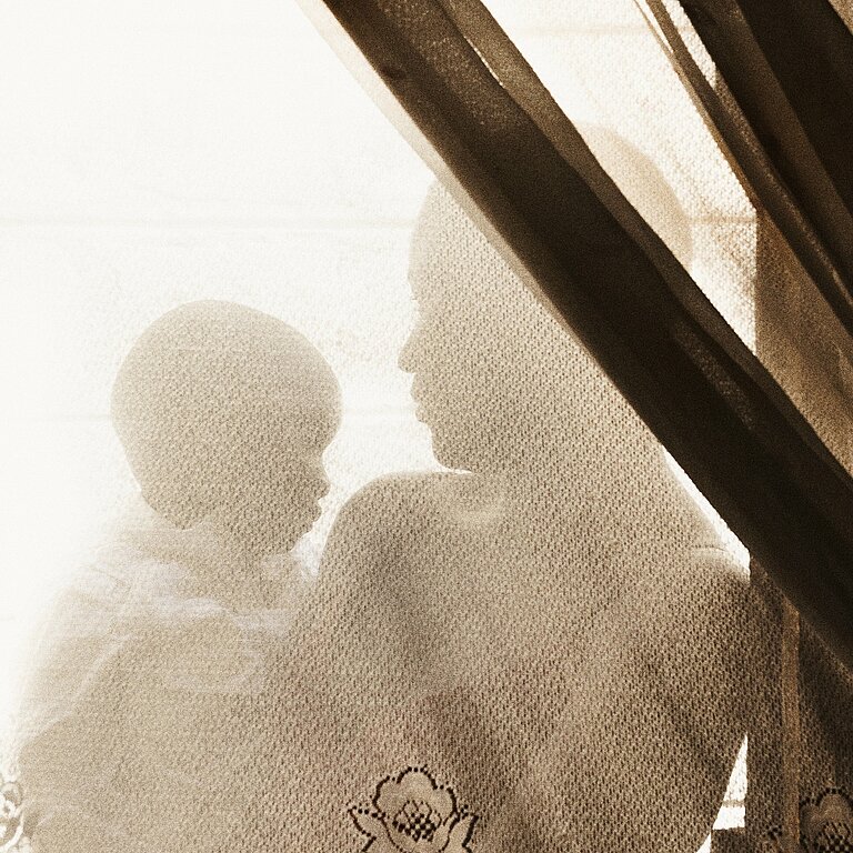 Eine Frau hält ein Baby auf dem Arm, sie stehen hinter einem durchsichtigen Vorhang, man sieht nur ihre Umrisse.