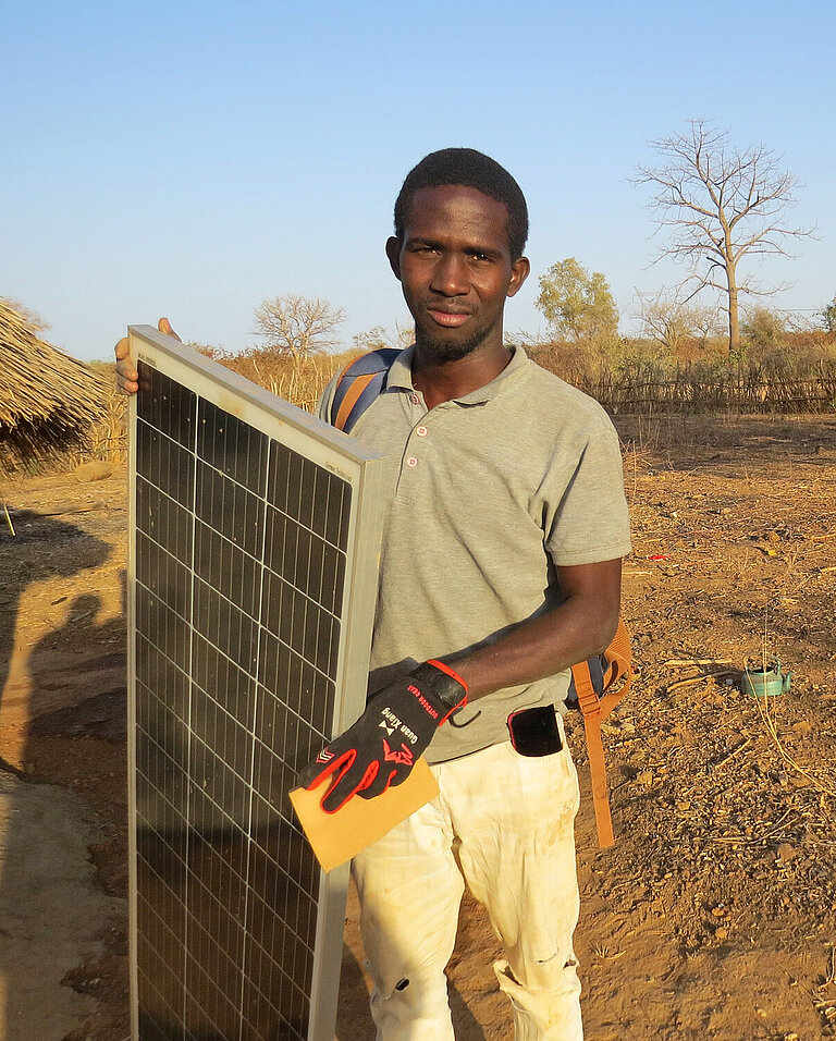 Ein junger afrikanischer Mann trägt ein Solarpanel