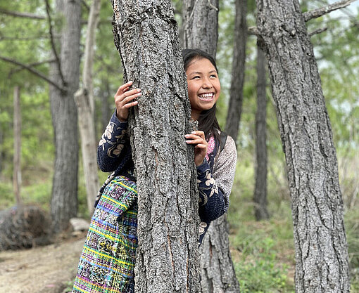 Kimberly hinter einem Baum lächelnd in einem Waldstück in Guatemala