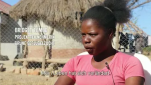 Bridget Tembo aus Sambia erzählt, wie das Projekt zur grünen Geflügelzucht ihr Leben verändert hat. Bridget Tembo, Projektteilnehmerin im Bereich grüne Geflügelzucht in Sambia, spricht über ihre Erfahrungen. Im Bild sitzt sie im Freien und sagt: „Mein Leben hat sich verändert.“