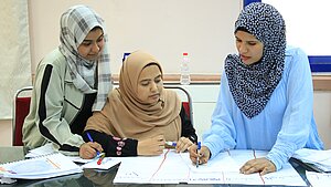 Drei junge Frauen arbeiten gemeinsam an einem Plakat mit handschriftlichen Notizen bei einem Menschenrechts-Workshop in Ägypten.