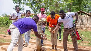 Mehrere Erwachsene testen gemeinsam eine neue Wasserpumpe in einem Dorf, das von Plan International unterstützt wird.