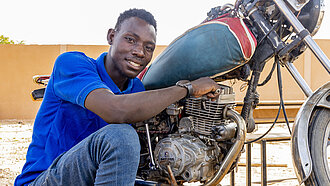 Junger Mann kniet vor einem Motorrad