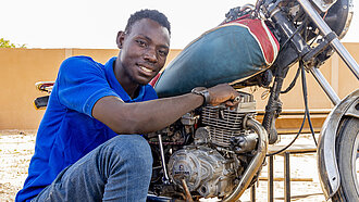 Junger Mann kniet vor einem Motorrad