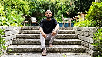 Ein Mann sitzt in inem Garten auf einer Treppe.