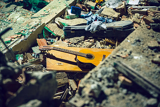 In den Trümmern eines eingestürzten Hauses liegen eine Gitarre und weitere Gegenstände der Menschen, die in dem Gebäude gelebt haben
