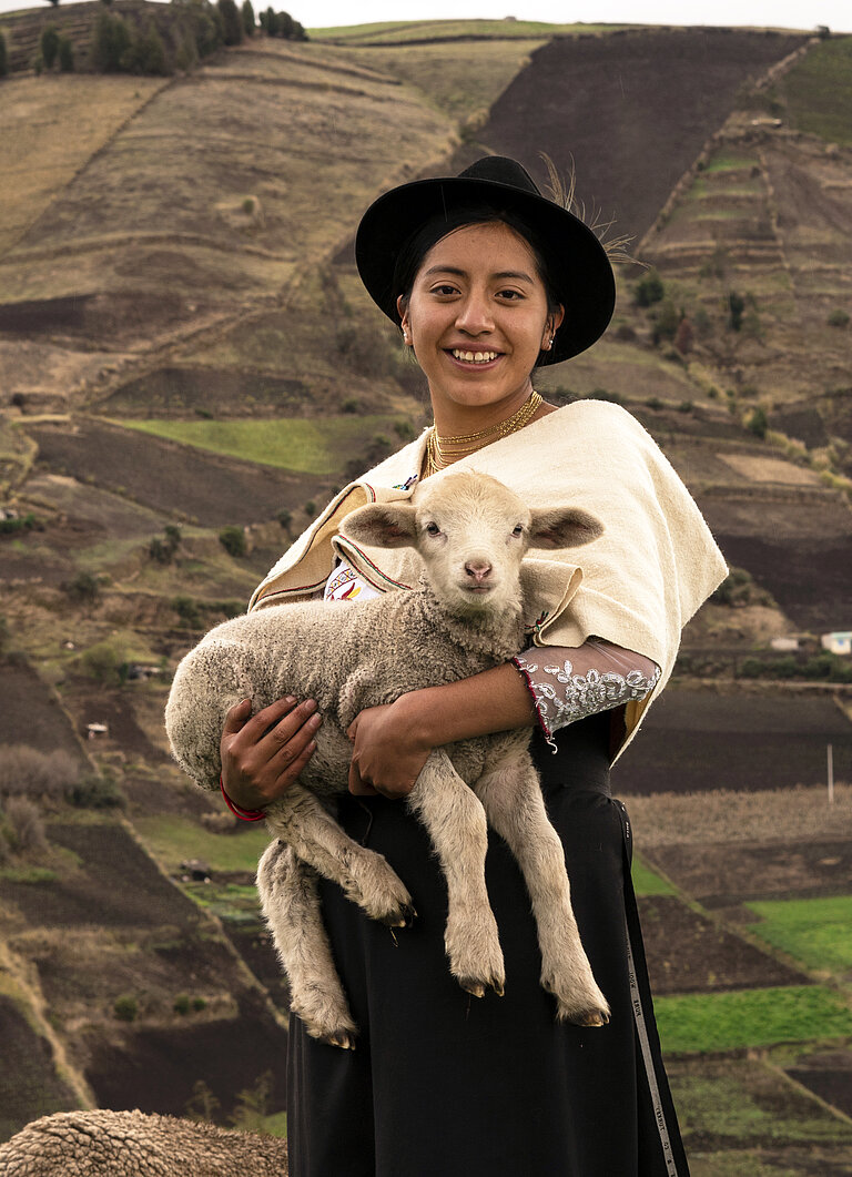 Junge Frau in hügeliger Landschaft mit Lamm auf dem Arm