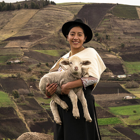 Junge Frau in hügeliger Landschaft mit Lamm auf dem Arm