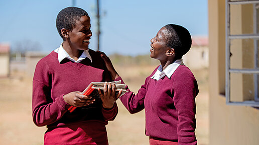 Zwei Kinder in roter Schuluniform lachen einander an.