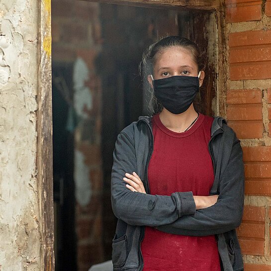 Lilian trägt eine schwarze Maske und verschränkt die Arme.