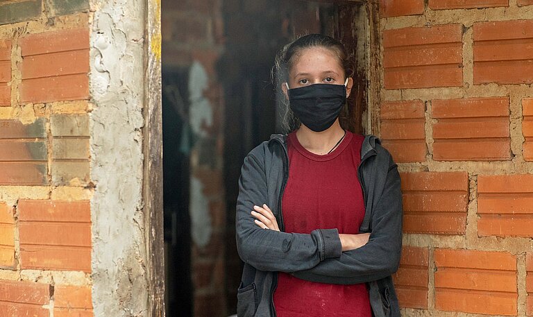 Lilian trägt eine schwarze Maske und verschränkt die Arme.